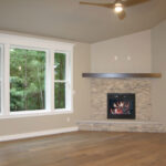 1502 Maple Hills Great Room. Stacked Stone Corner Fireplace to Mantel Height with Raised Hearth Extension. Boxed Maple Beam Style Mantel. Window with Painted Trim, Extended Sill, and Built-Up 3-Piece Head Trim with Crown Molding. Luxury Vinyl Plank Floors. Cathedral Ceiling.