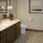 395 Whispering Creek Main Bathroom Vanity. Stained Flat Panel Maple Cabinet. Granite Countertops. Wood Framed Mirror. Tile Flooring.