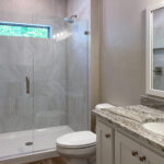 7714 Saint Andrews Main Bathroom. Granite Countertops. Painted Flat Panel Cabinets. Tiled Shower with Fiberglass Base and Heavy Glass Enclosure. Transom Window in Shower.