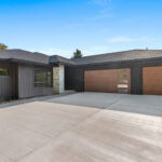 7736 Turnberry Modern Exterior. Black Vertical Board & Batten Siding. Oak woodgrain Overhead Garage Doors,