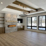 N3101 Right of Way Road Great Room. Stacked Stone Linear Modern Fireplace. Built-in Cabinets with Floating Shelves. Black windows with plastered drywall returns. Tray ceiling with stained maple wood beams. Luxury vinyl plank floors. 4-panel interior doors.