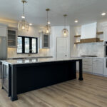 N3101 Right of Way Road Kitchen. Gray painted cabinets with black painted island. Plastered range hood with wood trim. Tiled backsplash. Black windows with plasted drywall returns. Luxury vinyl plank flooring. Under-counter refrigerator beverage center. Granite countertops. Floating shelves. 4 panel interior doors.