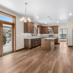 3597 E Hank Kitchen + Dining. Stone Countertops. Stained Maple Custom Cabinets. Under-Cabinet Range Hood. Pella Patio Door with Blinds in Glass. Herringbone Pattern Tiled Backsplash. Luxury Vinyl Plank Floors.