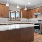 3597 E Hank Kitchen. Stone Countertops. Stained Maple Custom Cabinets. Under-Cabinet Range Hood. Bay Window. Herringbone Pattern Tiled Backsplash. Luxury Vinyl Plank Floors.