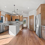3320 Cottage Hill Kitchen. Stained Maple Perimeter Cabinets with Painted White Island. Farmhouse Apron-Front Sink. Granite Countertops. Tiled Backsplash. Luxury Vinyl Plank Floors.