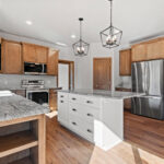 3320 Cottage Hill Kitchen. Stained Maple Perimeter Cabinets with Painted White Island. Farmhouse Apron-Front Sink. Granite Countertops. Tiled Backsplash. Luxury Vinyl Plank Floors.