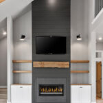 704 Royal St Pats Shiplap Fireplace. Black Painted Shiplap (Sherwin-Williams Iron Ore SW-7069) Fireplace Surround with Mitered Corners and Reclaimed Hewn Timber Mantel. Stained Maple Floating Shelves. TV Above Fireplace. Luxury Vinyl Plank Flooring. Hewn Timber Ceiling Beams at Vaulted Ceiling. Black Windows with White Painted Trim.