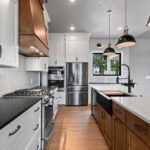 704 Royal St Pats Kitchen. Painted Perimeter Cabinets with Stained Maple Island and Custom Wood Hood. Pendant Lights. Under-Counter Beverage Center Refrigerator. Interior Transom. White Vertical Picket Tiled Backsplash. Glass Doors Above Upper Cabinets. Hewn Timber Ceiling Beams. Calacatta Prado Quartz with Black Pearl Brushed Granite Countertops.