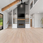 704 Royal St Pats Living Room. Black Painted Shiplap (Sherwin-Williams Iron Ore SW-7069) Fireplace Surround with Mitered Corners and Reclaimed Hewn Timber Mantel. Stained Maple Floating Shelves. TV Above Fireplace. Luxury Vinyl Plank Flooring. Hewn Timber Ceiling Beams at Vaulted Ceiling. Black Windows with White Painted Trim.