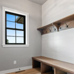 704 Royal St Pats Mud Room. Stained maple bench with coat hooks & shelf. Painted white shiplap planks. Black window with painted white trim.