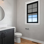 704 Royal St Pats Powder Room. Black Vanity Cabinet with White Stone Countertops. Circular Black Metal Frame Mirror.