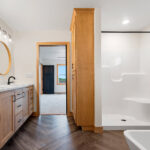 6170 Saint Patrick Owners Bathroom Vanity. Tiled Floors with Herringbone Pattern. Free-Standing Tub. Fiberglass Shower Module. Built-In Cabinet Linen. Round Wood Framed Mirrors.