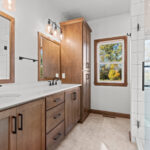 2960 Park Rd Owners Bathroom + Tiled Shower. Stained maple vanity cabinet with white quartz countertops. Vinyl tile flooring. Tiled shower walls with heavy glass enclosure.