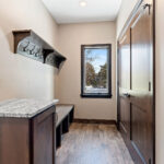 2966 Sugar Bush Mud Room. Stained knotty alder cabinets. Fantasy blue leathered granite countertops. Vinyl plank floors. Bench with coat hooks.