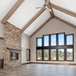 2966 Sugar Bush Great Room + Fireplace. Eldorado "Mountain Ledge Bitter Root" stone fireplace surround with steel mantel. Knotty alder stained cabinets. Cathedral ceiling with window wall and hewn timber ceiling beams. Adura Rigid Plank "Dockside Drift" luxury vinyl plank floors.