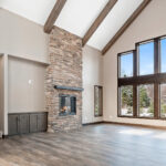 2966 Sugar Bush Great Room + Fireplace. Eldorado "Mountain Ledge Bitter Root" stone fireplace surround with steel mantel. Knotty alder stained cabinets. Cathedral ceiling with window wall and hewn timber ceiling beams. Adura Rigid Plank "Dockside Drift" luxury vinyl plank floors.