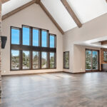 2966 Sugar Bush Great Room + Fireplace. Eldorado "Mountain Ledge Bitter Root" stone fireplace surround with steel mantel. Knotty alder stained cabinets. Cathedral ceiling with window wall and hewn timber ceiling beams. Adura Rigid Plank "Dockside Drift" luxury vinyl plank floors.