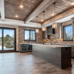 2966 Sugar Bush Kitchen + Dining. Eldorado "Mountain Ledge Bitter Root" backsplash wall stone. Knotty alder stained cabinets with wide plank island. Tray ceiling with weathered shiplap planks and hewn timber beams. Stoll black riveted steel custom range hood. Adura Rigid Plank "Dockside Drift" luxury vinyl plank floors. Lennon leathered granite countertops. Under-counter beverage centers. Reclaimed barn wood sliding barn door.