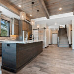 2966 Sugar Bush Kitchen. Eldorado "Mountain Ledge Bitter Root" backsplash wall stone. Knotty alder stained cabinets with wide plank island. Tray ceiling with weathered shiplap planks and hewn timber beams. Stoll black riveted steel custom range hood. Adura Rigid Plank "Dockside Drift" luxury vinyl plank floors. Lennon leathered granite countertops. Under-counter beverage centers. Reclaimed barn wood sliding barn door.