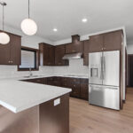 398 Red Tail Kitchen. Mid-Century Modern Revival. Interior Brick Walls. Flush Slab-Front Stained Maple Cabinets. Built-In Wall Oven. Electric Cooktop. Under-Cabinet Range Hood. Luxury Vinyl Plank Floors.