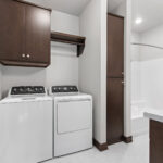 398 Red Tail Main Bathroom & Laundry. Mid-Century Modern Revival. Flush Slab-Front Stained Maple Cabinets. Linen with Countertop Above. Wood-Framed Mirror.