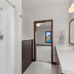 398 Red Tail Owners Bathroom. Mid-Century Modern Revival. Flush Slab-Front Stained Maple Cabinets. Linen with Countertop Above. Wood-Framed Mirror. Hand Shower.