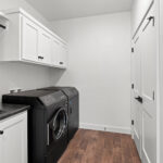 7730 Prestwick Laundry. White Painted Woodwork & Cabinetry. Black Washer & Dryer. Luxury Vinyl Plank Floors. Upper Cabinets above Washer & Dryer. Hanging Pole above Sink Base Cabinet.
