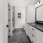 7730 Prestwick Owners Bathroom. Black Granite Countertops. White Painted Woodwork Bathroom Vanity. Black Wood Mirror Frame. Grouted Vinyl Tile Floors. Tiled Shower with Heavy Glass Enclosure.