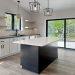 8241 Peil Ln Kitchen. White Painted Perimeter Cabinets with Black Countertops and Black Stained Maple Island with White Stone Countertops. Natural Maple Floating Shelves with LED Strip Lights. Tiled Backsplash. Luxury Vinyl Plank Floors. Black windows with plastered drywalled returns. Cathedral Ceiling.