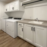 8241 Peil Ln Laundry. Top Load Washing Machine. Upper Cabinets above Washer & Dryer. Hanging pole & shelf above White Painted Laundry Utility Sink Cabinet.