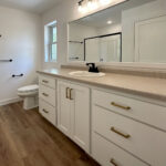8241 Peil Ln Owners Bathroom Vanity. White Painted Vanity Cabinet with Gold Hardware and Black Laminate Countertops. Wood-Framed Mirror.