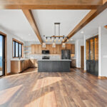 10510 Sugar Creek Kitchen & Dining. Custom maple cabinets, black island, quartz countertops, vinyl plank floors, ceiling beams, floating shelves, black interior windows over kitchen sink, under-cabinet lighting, tiled backsplash.