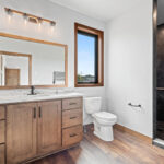 10510 Sugar Creek Owners Bathroom. Maple vanity cabinet with stone countertops, towel warming rack, walk-in tiled shower, wood-framed mirror, vinyl plank floors.
