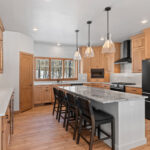 14421 N Paya Lake Rd Kitchen. Horizon Glossy "Mist" tiled backsplash to ceiling. Cortec Pro "Brookfield Maple" vinyl plank floors. Cascade granite and Silestone "Miami Vena" countertops. Corner Walk-In Pantry. Glacier White painted island with stained flat panel maple perimeter cabinets with floating shelves and glass doors. Microwave in corner cabinet. GE black slate appliances. Slide-in gas range. Under-counter beverage refrigerator.